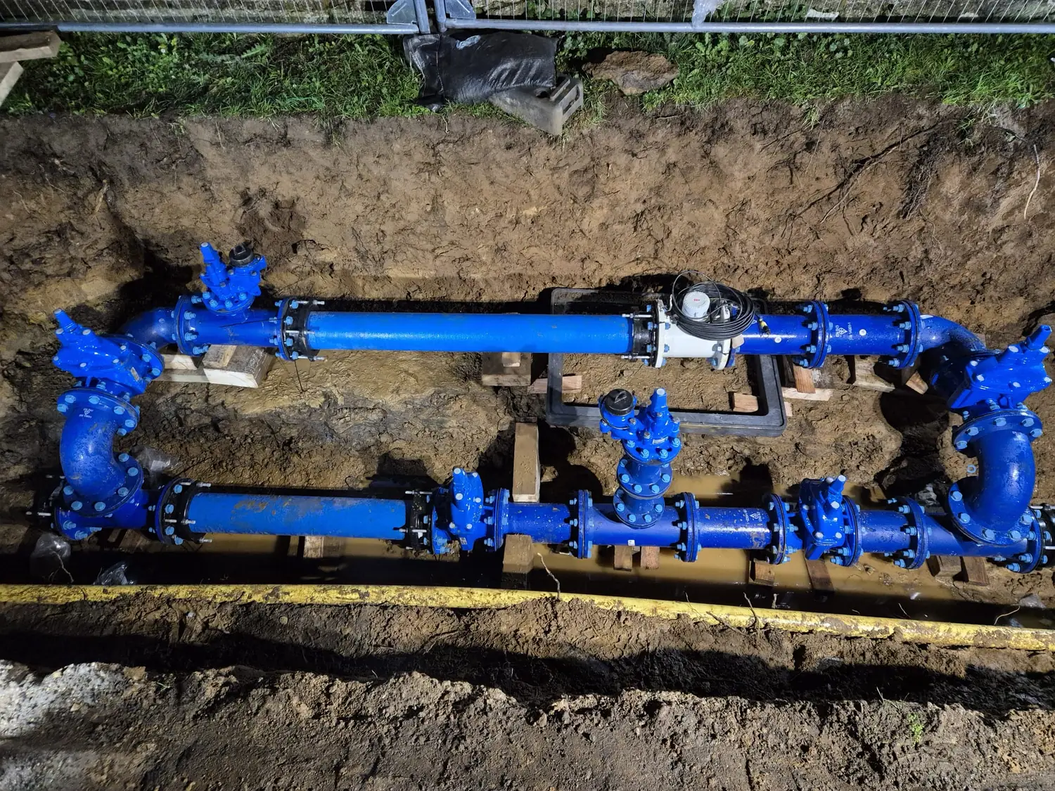 A new blue ductile-iron water main and valve assembly installed by Malling Utilities in an open trench at night in Kent